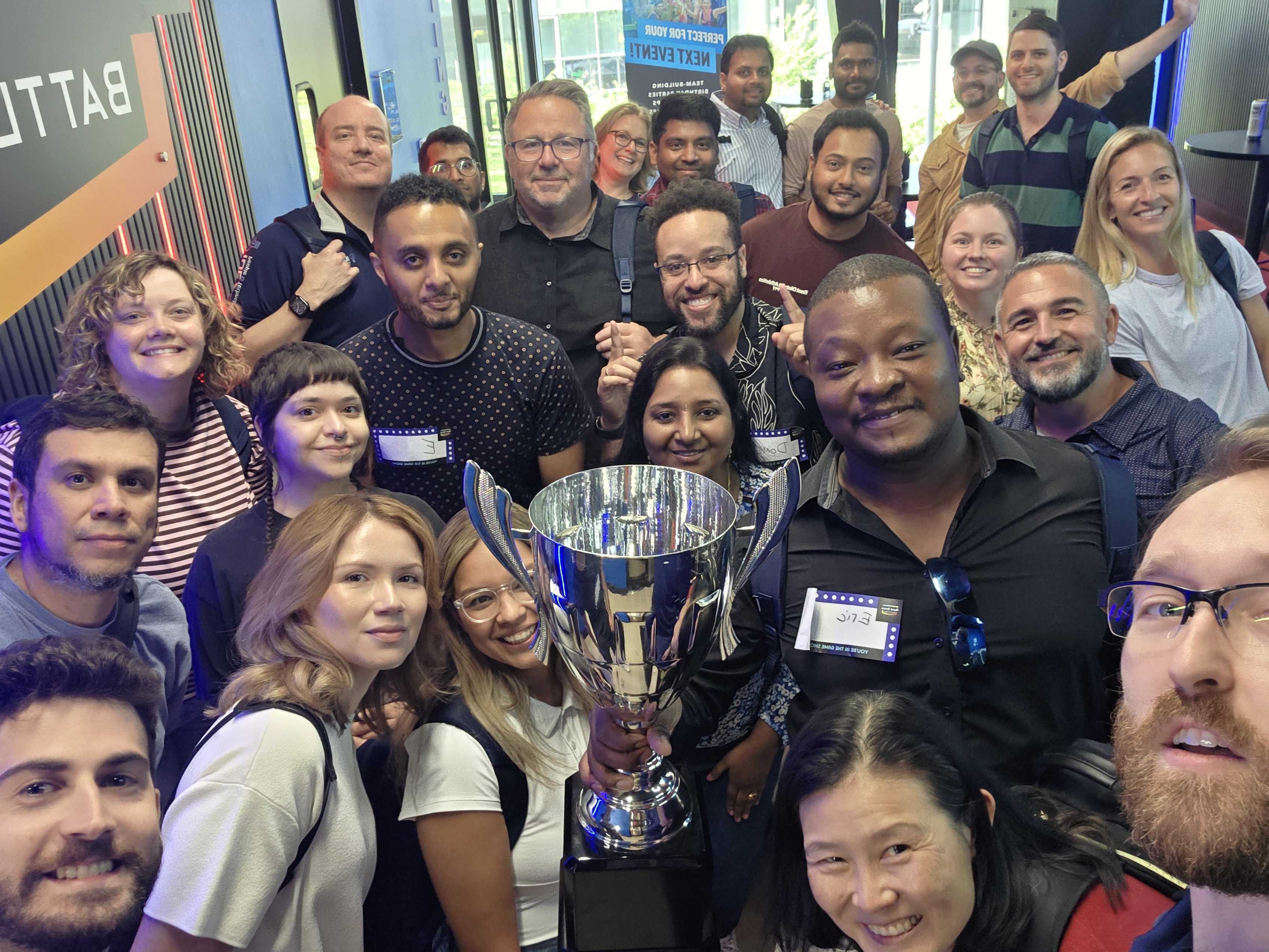 The IdeaCrew team crowded around a trophy at a company outing